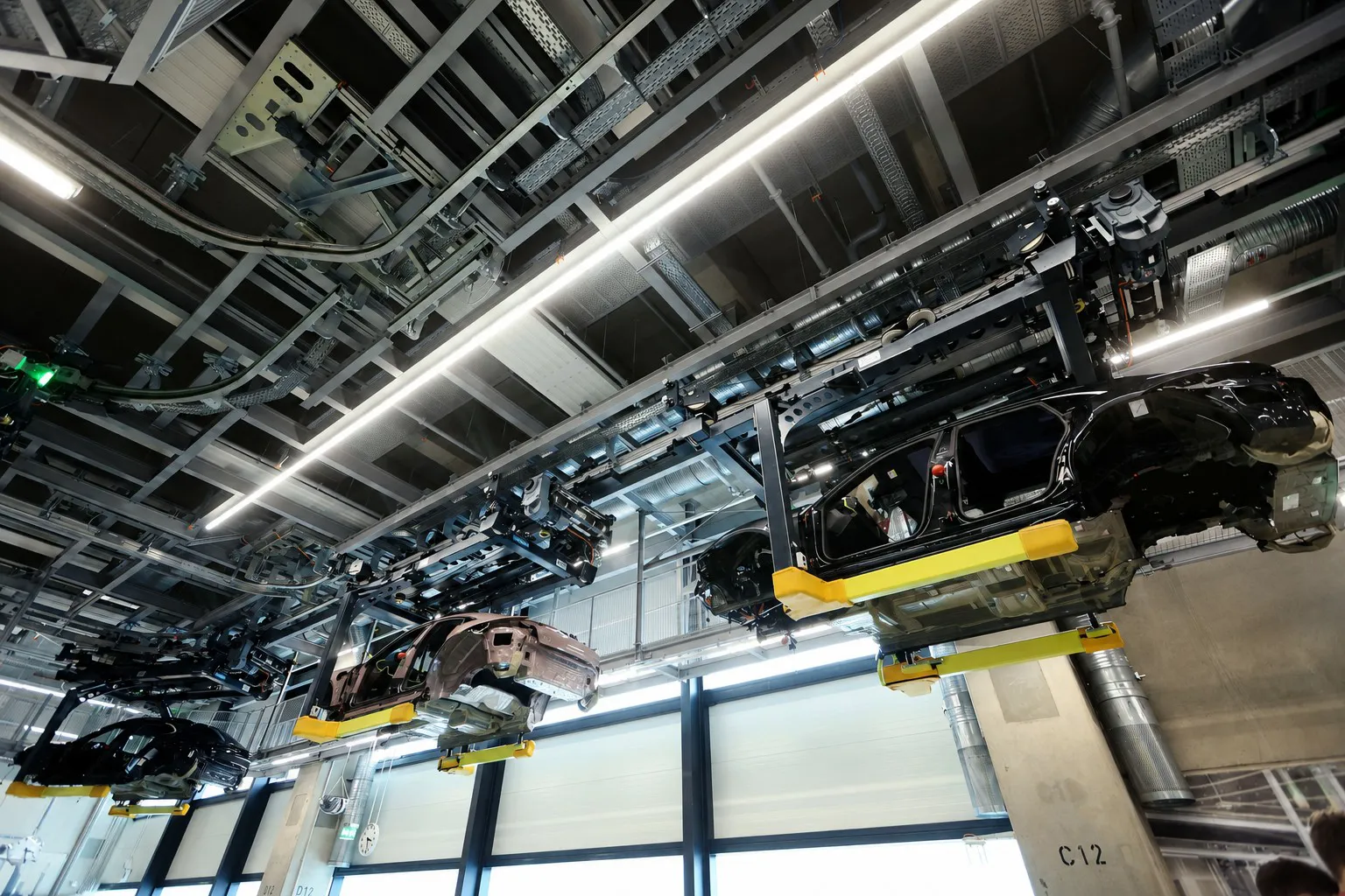 Electric car body shells carried in overhead conveyor cradles along a factory ceiling line