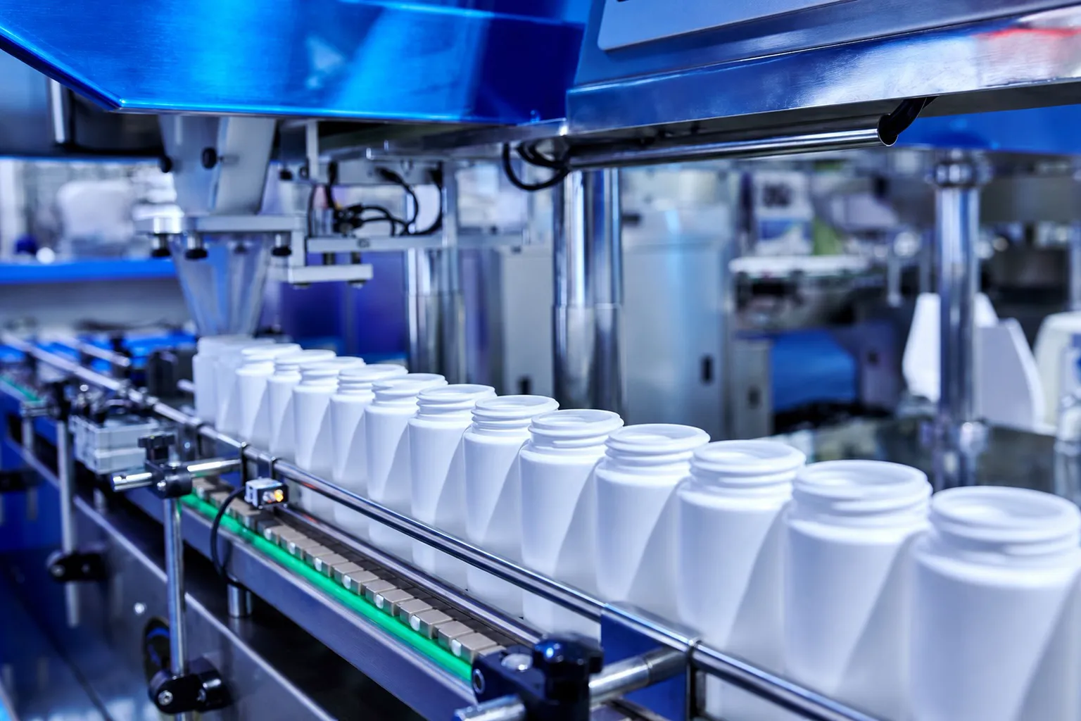 A row of white plastic bottles travelling along a conveyor on an automated filling line