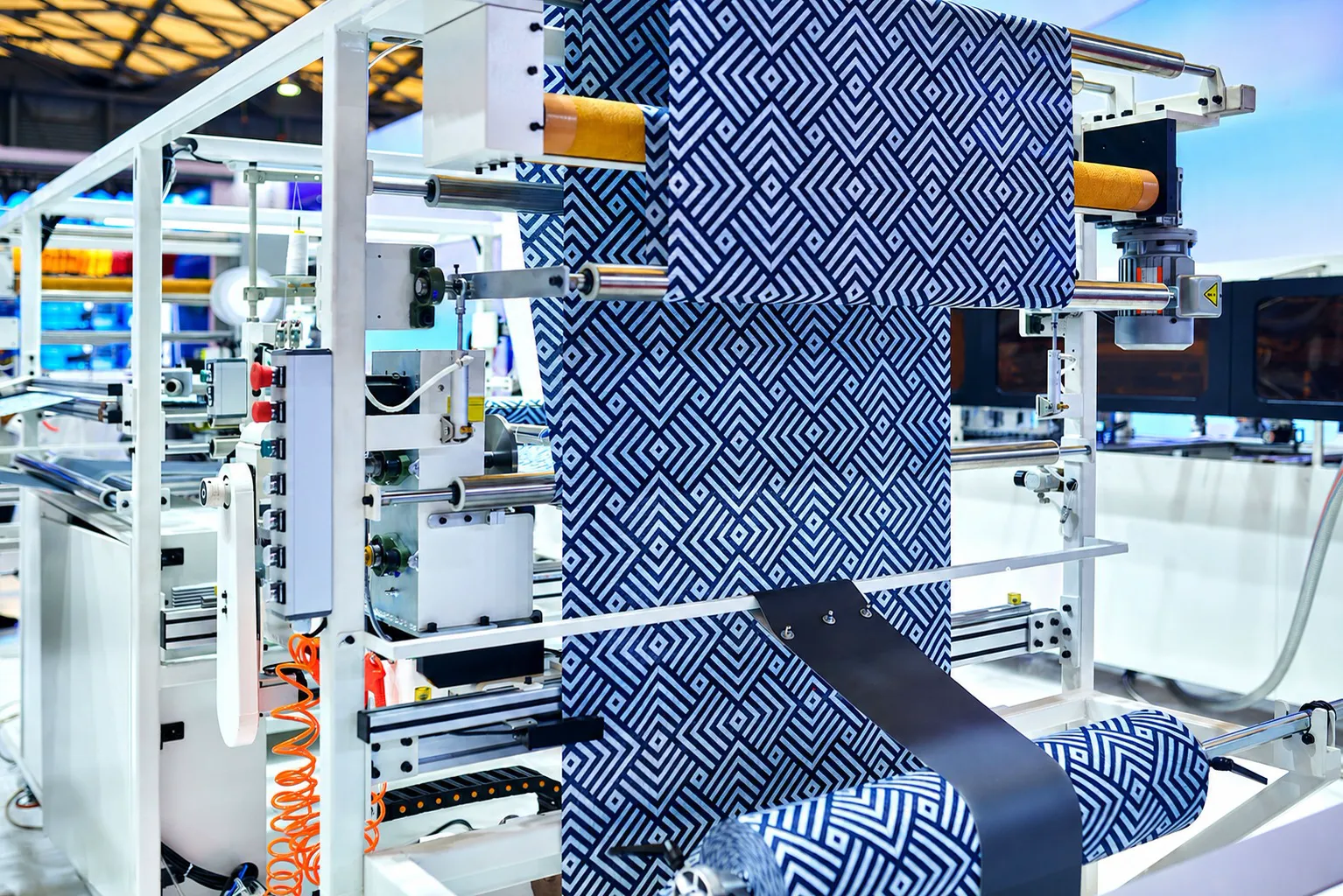 A bolt of patterned blue-and-white furnishing fabric running through a textile finishing machine